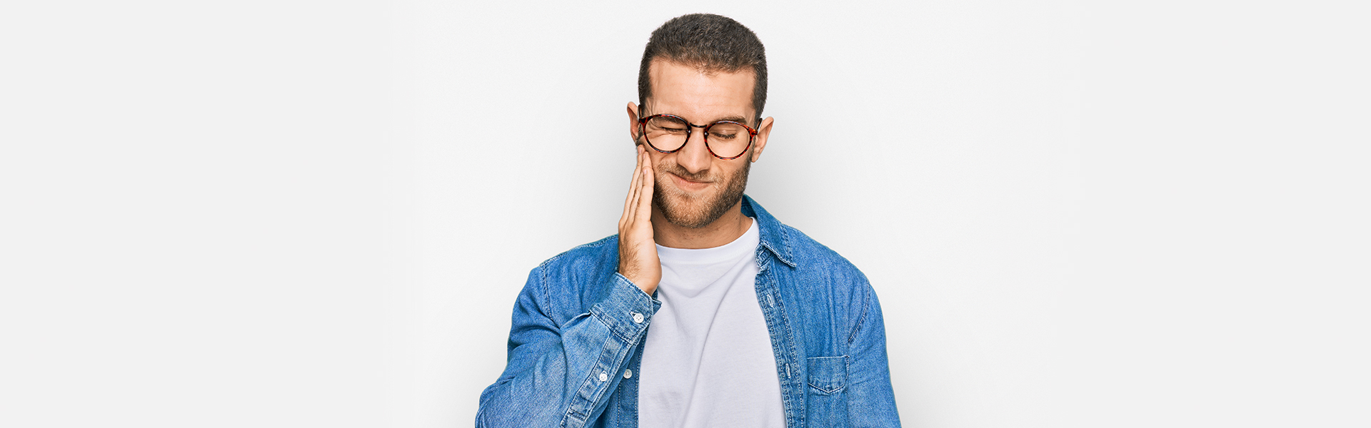 A man with eyeglasses is experiencing a toothache